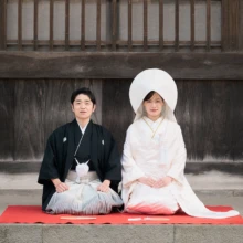 建長寺の歴史ある木造建築を背景に、白無垢と黒紋付で残す正統派の和装フォトウェディング|縁グラフィの姉妹ブランドLuca 建長寺の木造建築を背景に、赤い毛氈の上で正座する綿帽子姿の花嫁と黒紋付姿の新郎