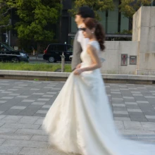 歩くふたりの動きをあえてブレとして残した、躍動感のあるウェディングフォト。丸の内の都会的な街並みを舞台に、ドレスの流れまで印象的に切り取った一枚です|縁グラフィの姉妹ブランドLuca 東京・丸の内の街並みで、ウェディングドレス姿の花嫁と新郎が歩く姿をスローシャッターで撮影した前撮り写真