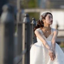 丸の内に差し込む夕方の光を活かした、花嫁のソロショット。柔らかな光と陰影がドレスの質感や表情を引き立てる、落ち着きのあるウェディングフォト|縁グラフィの姉妹ブランドLuca 東京・丸の内の街並みで、夕方の光を受けながら座るウェディングドレス姿の花嫁を撮影した前撮り写真
