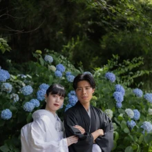 初夏の三溪園を彩る紫陽花に囲まれて。白無垢と黒紋付が鮮やかな緑と青い花々に映える、季節感あふれる和装フォトウェディング|縁グラフィの姉妹ブランドLuca 横浜・三溪園に咲く青い紫陽花を背景に、白無垢姿の花嫁と黒紋付姿の新郎が寄り添う和装ウェディングフォト