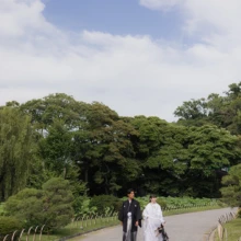 青空と豊かな緑が広がる三溪園をふたりで歩く一枚。開放感ある日本庭園で残す和装フォトウェディング|縁グラフィの姉妹ブランドLuca 横浜・三溪園の緑豊かな日本庭園を歩く、白無垢姿の花嫁と黒紋付姿の新郎の和装ウェディングフォト