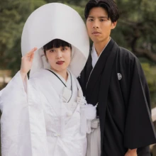 綿帽子と白無垢、黒紋付で凛と佇むふたり。三溪園の豊かな緑を背景に残す、伝統美を感じる和装フォトウェディング|縁グラフィの姉妹ブランドLuca 横浜・三溪園で綿帽子と白無垢姿の花嫁、黒紋付姿の新郎を撮影した和装ウェディングフォト