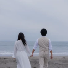 由比ヶ浜の海を眺めながら手をつなぐ、ふたりの自然なウェディングフォト|縁グラフィの姉妹ブランドLuca 由比ヶ浜の海を背景に、手をつないで佇むウェディングドレス姿の花嫁と新郎