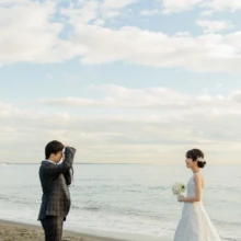 鎌倉和洋装S様・S様 2019.12.23 穏やかな海を背景に、カメラを構える新郎とウェディングドレス姿で向かい合う新婦の鎌倉フォトウェディング