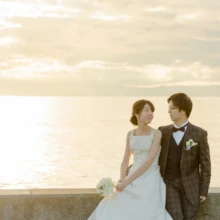 鎌倉和洋装S様・S様 2019.12.23 夕日に輝く海を背景に、ウェディングドレスの新婦とタキシードの新郎が見つめ合う鎌倉フォトウェディング