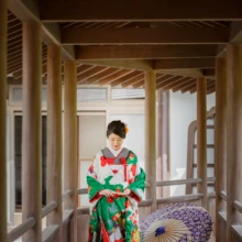 鎌倉 和装 T様・U様 2020.09.29 光明寺の回廊で紫色の花柄和傘を傍らに置き、緑と赤の色打掛姿でうつむく新婦の全身