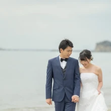鎌倉 和洋装 T様・Y様 2021.03.20 七里ガ浜の海辺で手をつなぎ、足元を見ながら寄り添うウェディングドレス姿の新婦と青いタキシード姿の新郎