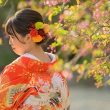 鎌倉 和洋装 T様・Y様 2021.03.20 赤い色打掛の鶴の文様と、赤や黄色の生花を飾った花嫁のまとめ髪を春の花とともに捉えた後ろ姿