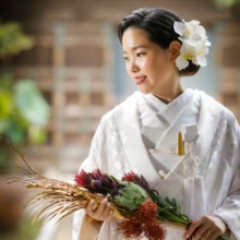 鎌倉 和装 M様・M様 2020.09.18 赤や深緑のブーケを持ち、白い花の髪飾りを合わせた白無垢姿の新婦の上半身