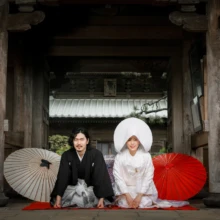 鎌倉 和装 M様・M様 2020.09.18 鎌倉の寺院の門前で、綿帽子姿の新婦と黒紋付袴の新郎が和傘を添えて正座する和装前撮り