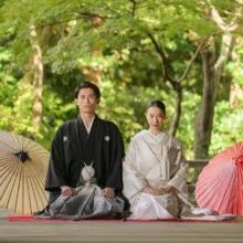 鎌倉 和装 N様N様 2020.11.02 妙本寺の本堂前で、黒紋付袴姿の新郎と白無垢姿の新婦が赤い毛氈に正座し、両側に白と赤の和傘を並べる