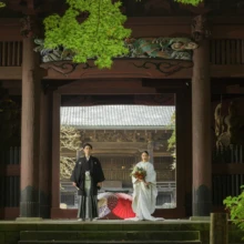 鎌倉 和装 N様N様 2020.11.02 妙本寺の山門を額縁のように捉え、白無垢姿の新婦と黒紋付袴姿の新郎が境内に立ち、足元に赤い和傘を置く
