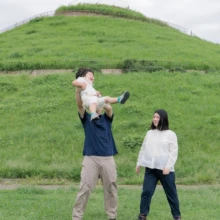 家族写真 M様 2025.09.21 緑の丘が広がる公園で、乳幼児を含む三世代の家族が肩を寄せて並ぶ秋のファミリーロケーション撮影
