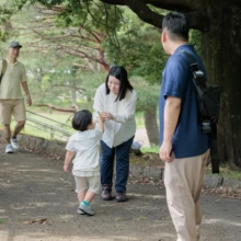 家族写真 M様 2025.09.21 木陰の園路で、母親の手を取る幼い子どもを父親と祖父が見守る家族の日常的なひととき