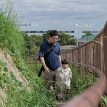 家族写真 M様 2025.09.21 街と海を見渡せる公園の階段を、幼い子どもの手を取りながら一緒に上る父親の後ろ姿
