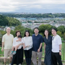 家族写真 M様 2025.09.21 高台から街並みを望む展望スペースで、乳幼児を囲んで横一列に並ぶ三世代の家族