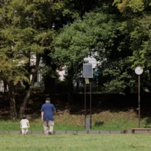 家族写真 M様 2025.09.21 秋の緑が残る広い公園の芝生を、手をつないで歩く父親と幼い子どもの小さな後ろ姿