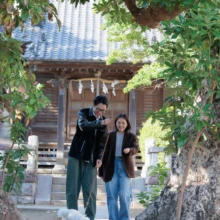 ペット・家族写真 H様 2025.11.15 大きな木に囲まれた神社の参道を、足元の白い小型犬と一緒に歩く夫婦の自然な様子