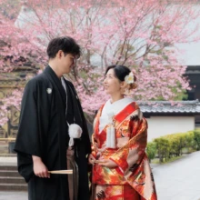 鎌倉 和装 M様・I様 2026.04.02 建長寺の淡い紅色の桜を背に、見つめ合って微笑む黒紋付袴の新郎と赤い色打掛の新婦の鎌倉和装前撮り