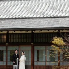 鎌倉 和装 T様・K様 2026.04.05 円覚寺の瓦屋根と長い縁側を大きく収め、白無垢の新婦と黒紋付袴の新郎が並ぶ全身の構図