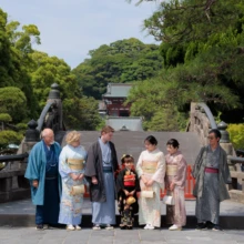 七五三撮影 I様 2026.06.01 鶴岡八幡宮で、黒い着物の女の子を中央に色とりどりの和装をまとった三世代の家族7人が並ぶ七五三撮影