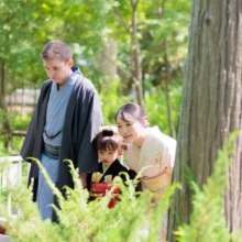 七五三撮影 I様 2026.06.01 鶴岡八幡宮の緑豊かな境内で、七五三の女の子と和装姿の両親が植物をのぞき込む自然なひととき