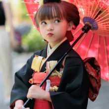 七五三撮影 I様 2026.06.01 赤い花柄の番傘を肩に添え、黒地の着物と赤い帯をまとった七五三の女の子の上半身