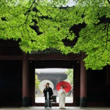 鎌倉 和装 I様・Y様 2026.07.05 鮮やかな新緑に包まれた妙本寺の山門で、黒紋付袴の新郎と白無垢の新婦が和傘を持って並ぶ姿