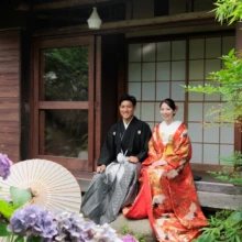 鎌倉 和装 I様・Y様 2026.07.05 アジサイが咲く鎌倉の古民家で、黒紋付袴の新郎と赤い色打掛の新婦が縁側に並んで正座する姿